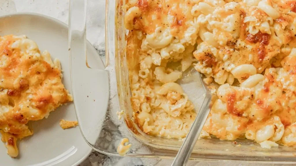 A casserole of baked mac and cheese with a plate of mac and cheese nearby.