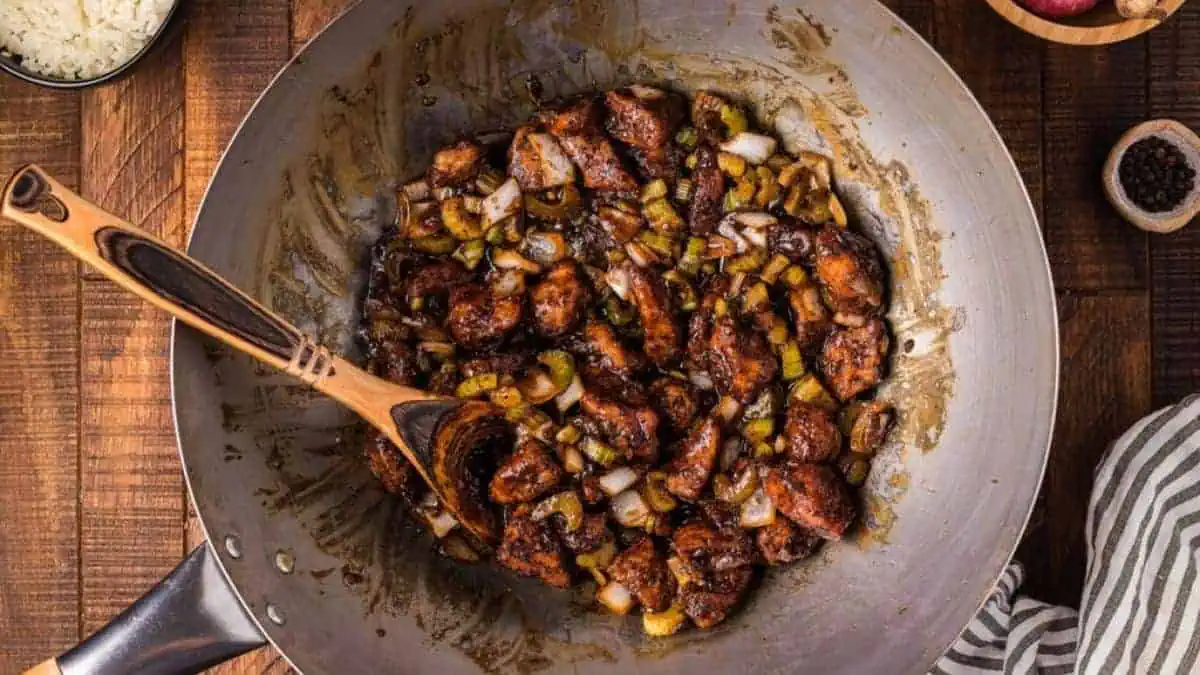 a skillet of black pepper chicken with a wooden spoon.