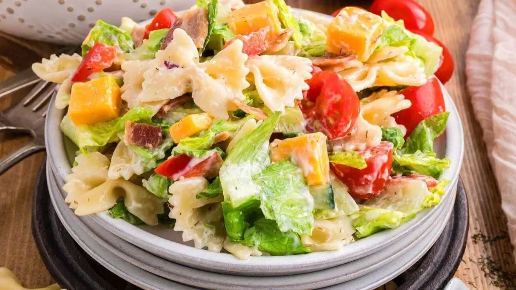 A plate of pasta salad with lettuce, tomato and bacon.
