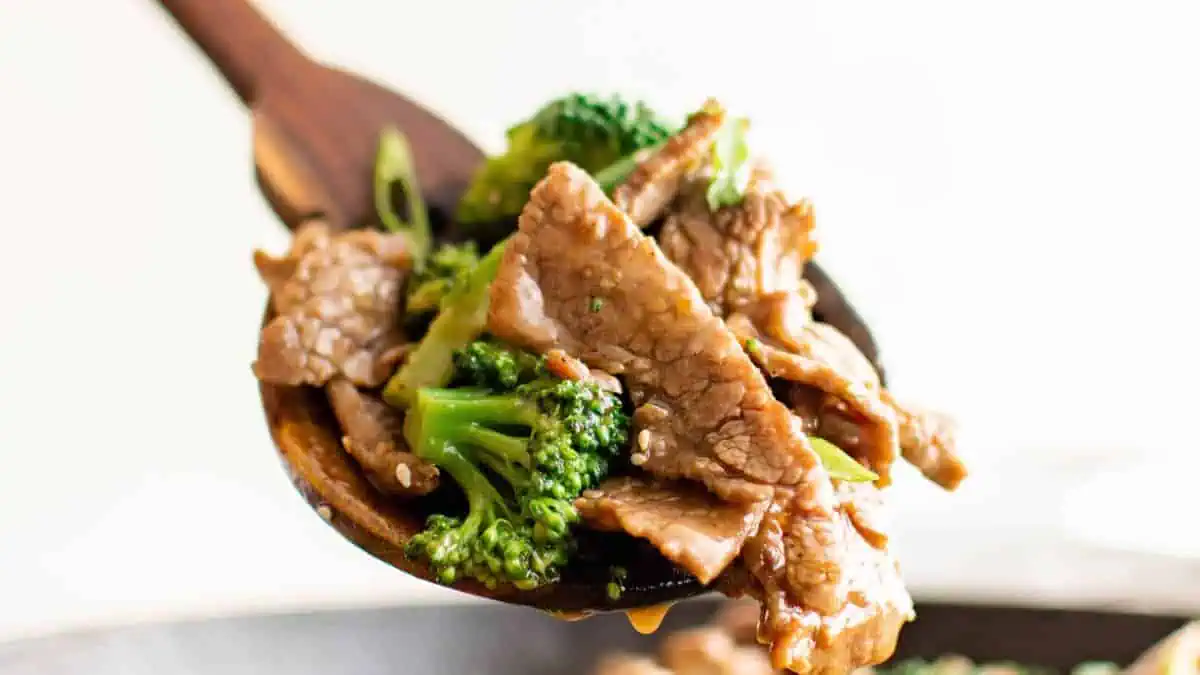 a spoon lifting beef and broccoli from a skillet