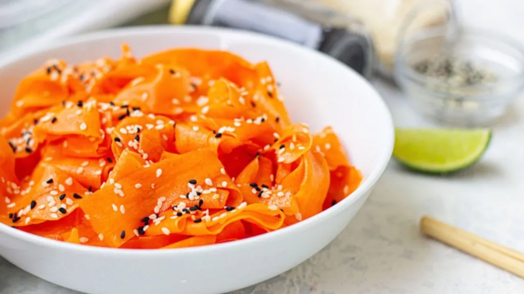 A bowl of thin carrot strips with sesame seeds over top.