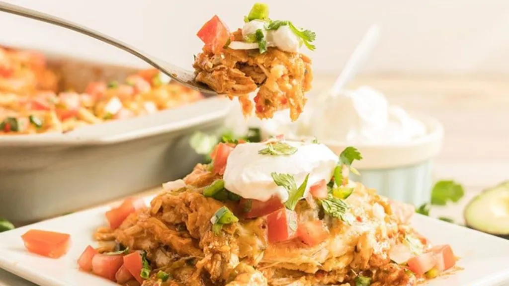 a plate with chicken enchilada casserole, with lettuce, tomato and sour cream over the top.