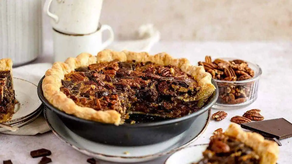 A pecan pie with chocolate chunks, with a slice cut out.