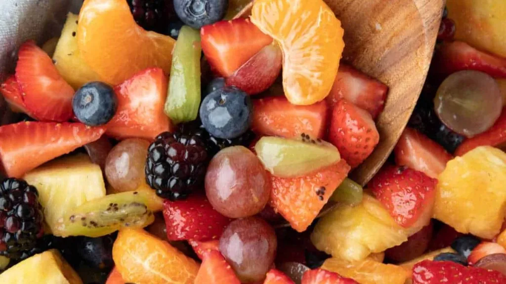 A bowl of fruit salad with a wooden spoon.