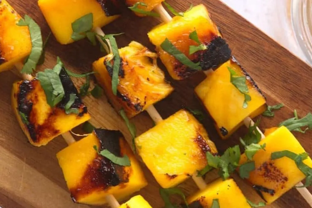 Skewers of grilled mango chunks on a cutting board.