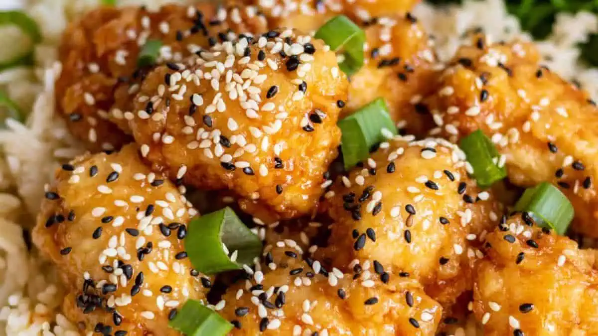 a plate of white rice topped with honey sesame chicken.