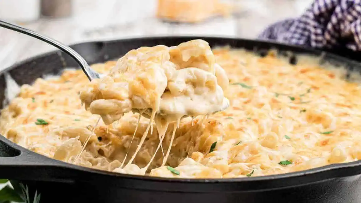 A skillet of creamy mac and cheese with a spoon lifting a serving out.