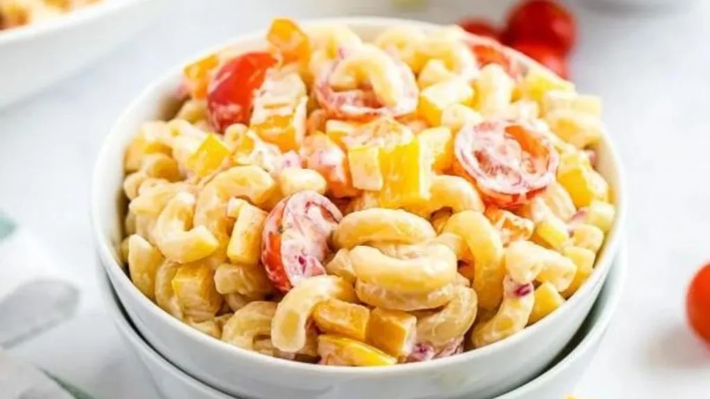 A bowl of macaroni salad with tomatoes and pepper chunks.