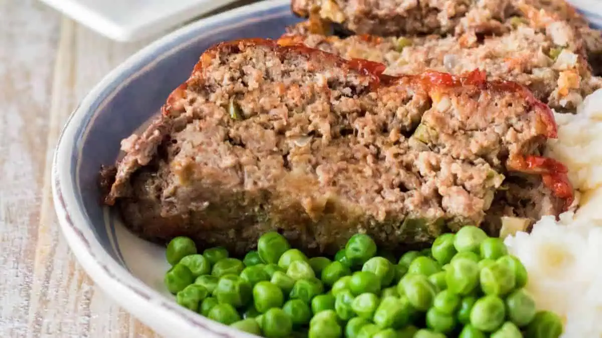 A plate of meatloaf, potatoes and peas