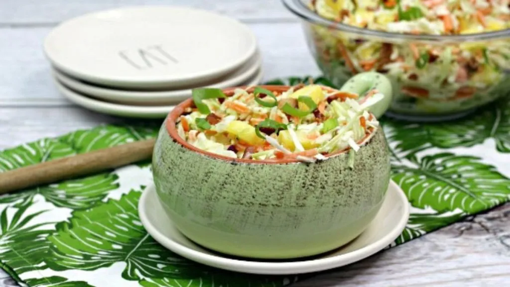 A bowl of coleslaw made southern style with bacon, green onions and pineapple chunks.