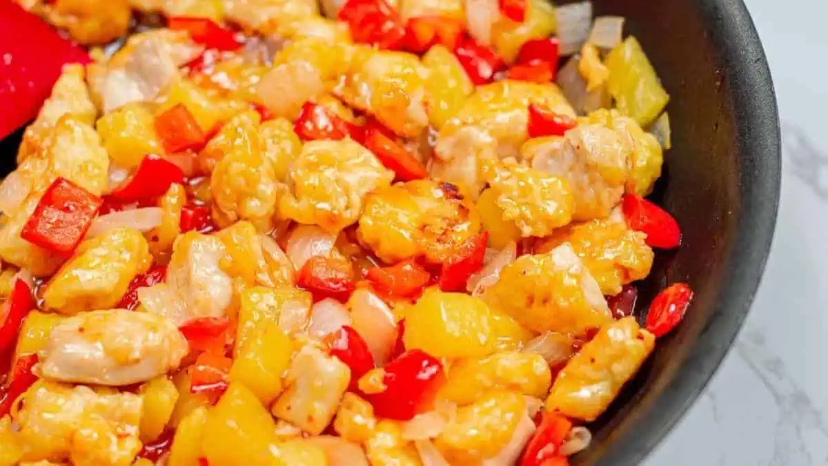 a bowl of pineapple, peppers, onions and saucy chicken chunks.