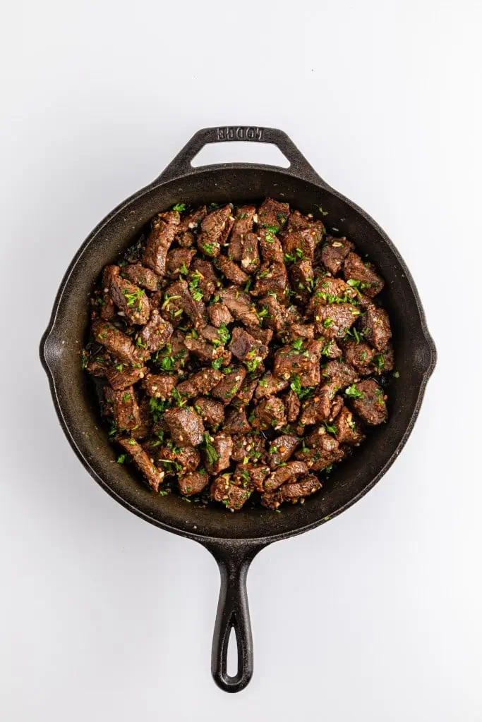 a delicious one pan recipe of seared sirloin garlic butter steak bites with fresh herbs in a black cast iron skillet