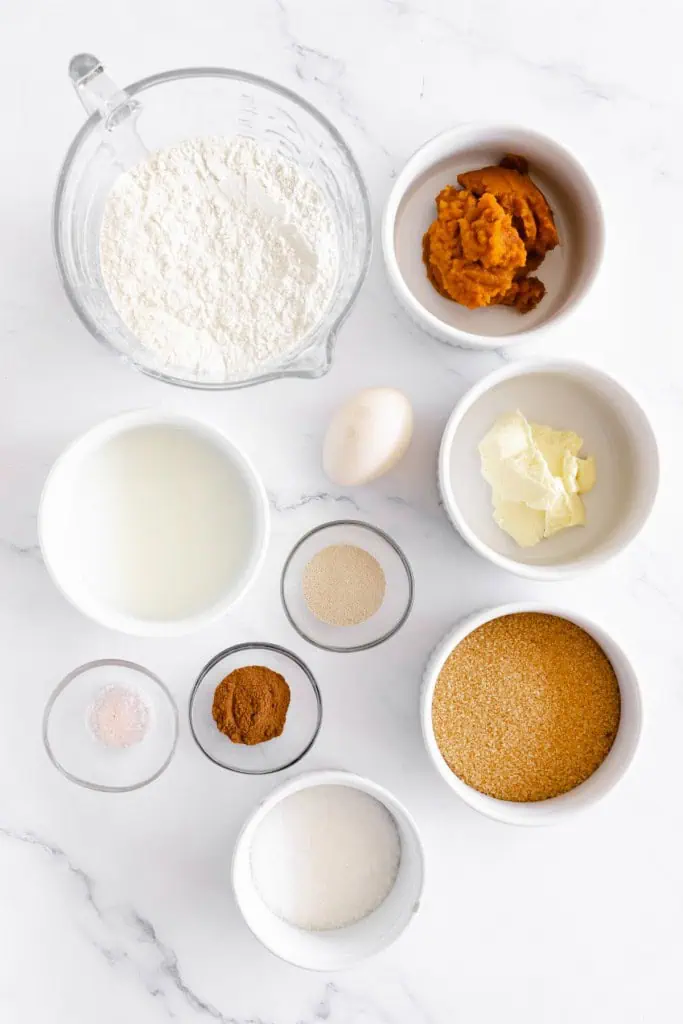 Ingredients for pumpkin cinnamon rolls on a white marble countertop.