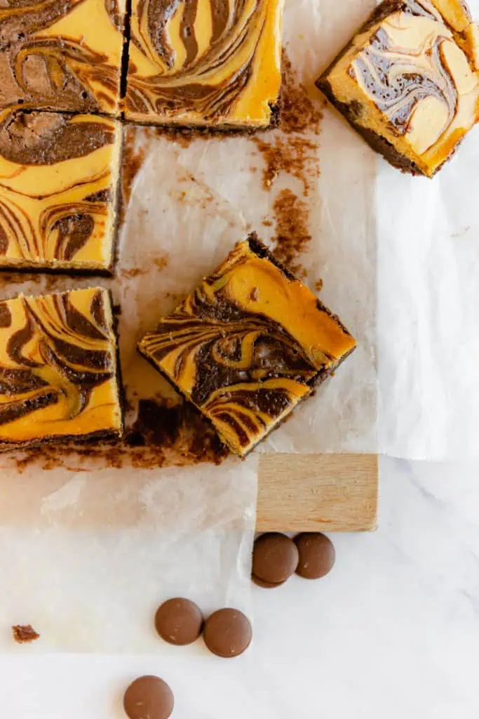 Close up of slices of pumpkin cream cheese brownies on top of parchment paper on a wooden kitchen board.
