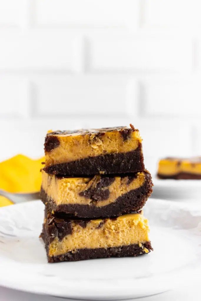 Stacked pumpkin cream cheese brownies on top of parchment paper.