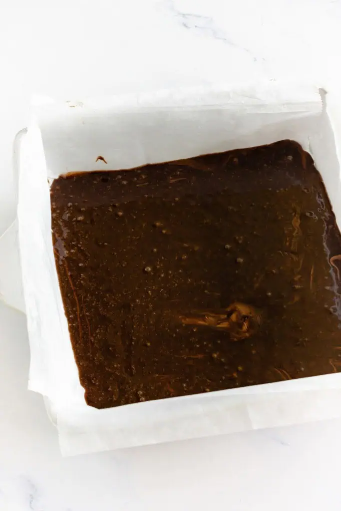Chocolate brownie batter poured into a parchment-lined baking pan.