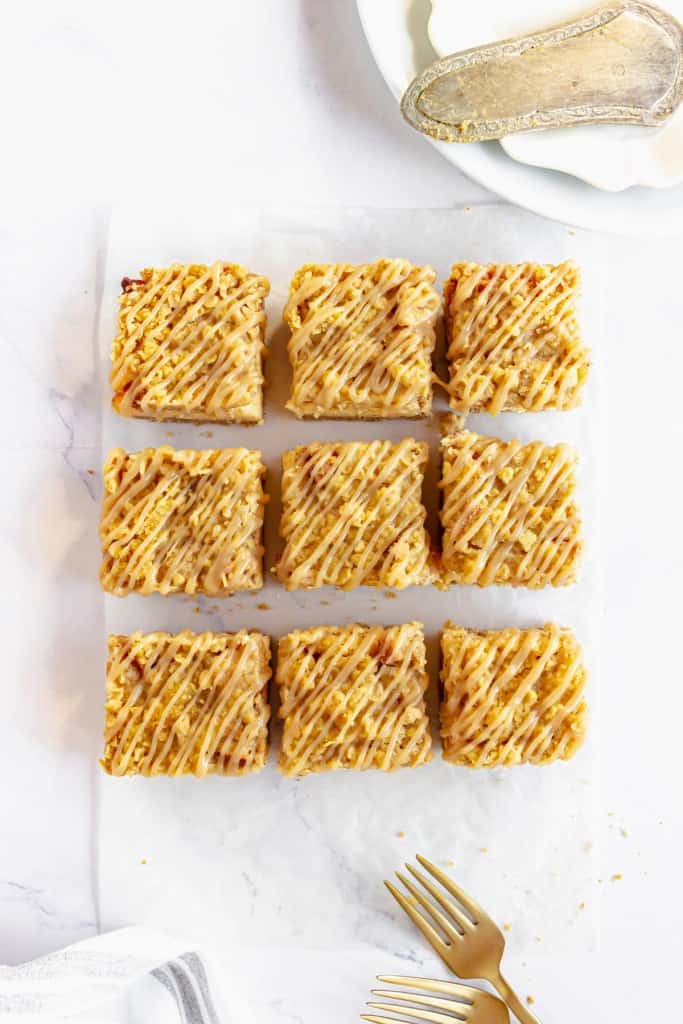 Overhead view of sliced apple cheesecake bars on parchment paper on a white marble countertop.