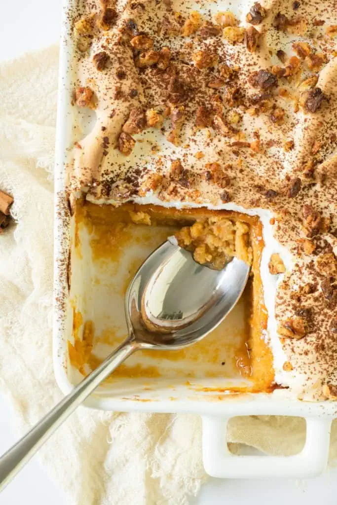 Close up of a slice of pudding removed from the casserole of sweet potato pudding with a large metal serving spoon.