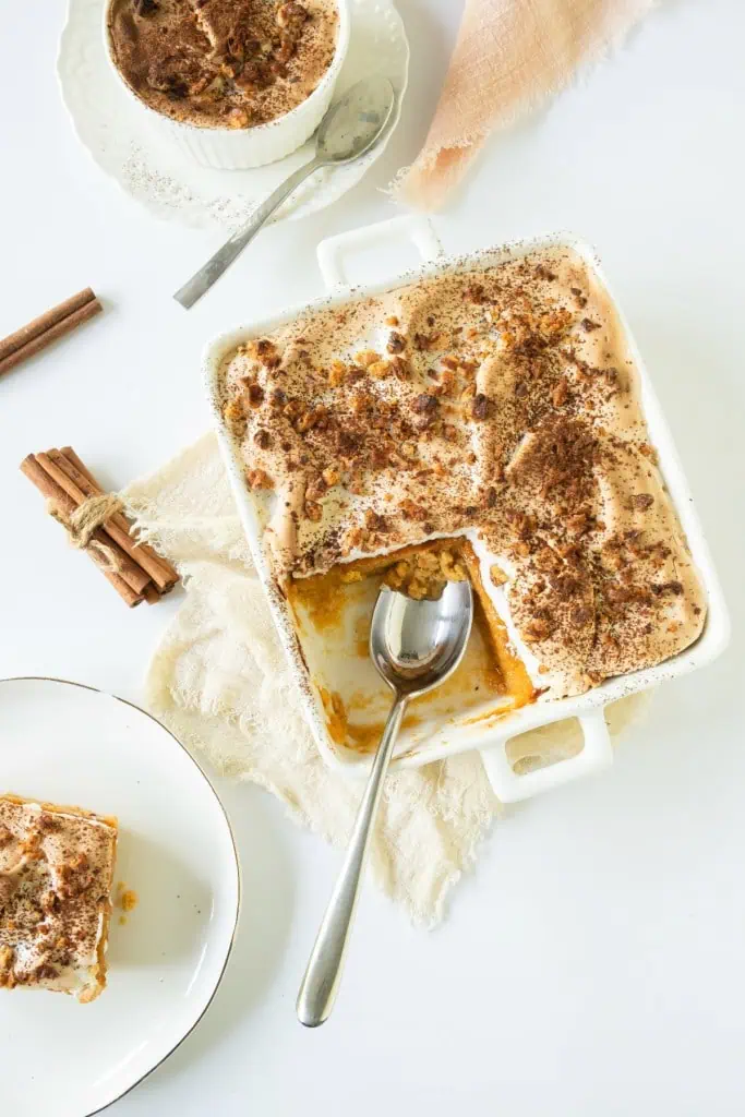 A slice of sweet potato pudding removed from the casserole dish, a large serving spoon in the casserole dish, a small serving plate with a slice of pudding, and a single ramekin filled with sweet potato pudding.