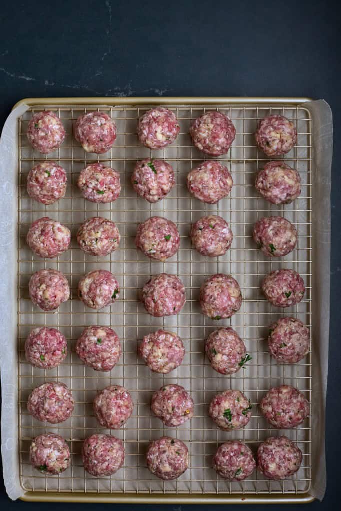 Large baking tray lined with parchment paper, metal grid placed over the parchment paper with the meatballs placed equally apart. 
