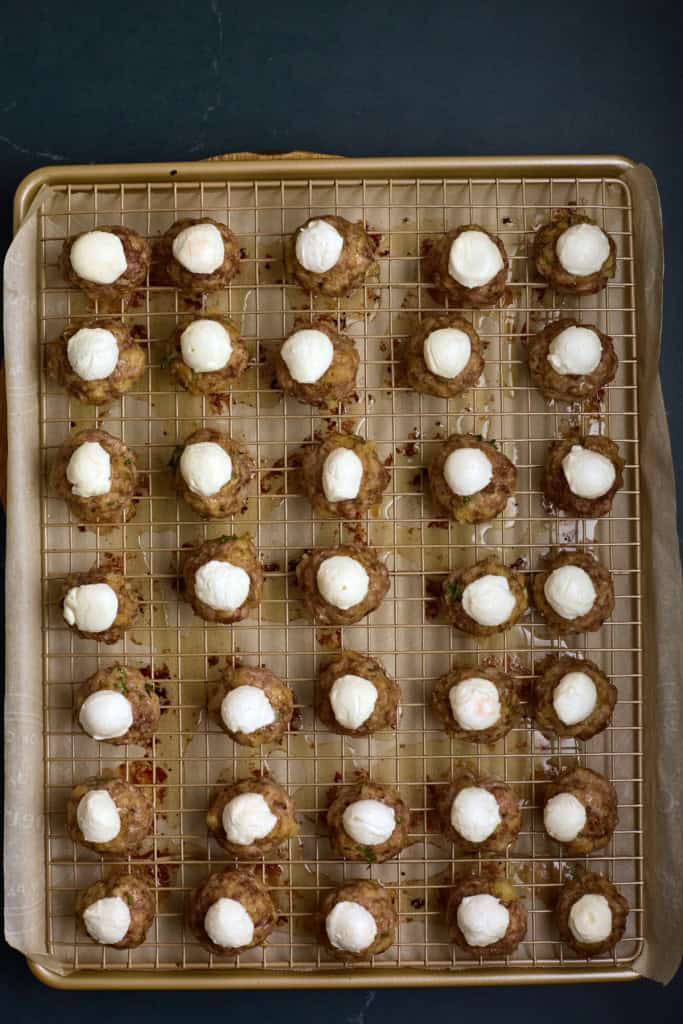 Baked meatballs on a baking sheet, topped with halved mozzarella cheese balls.