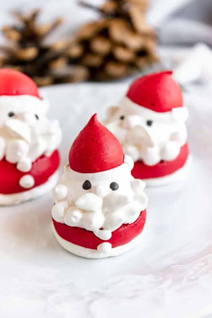 Gros plan de trois meringues de Père Noël assemblées sur une assiette blanche.