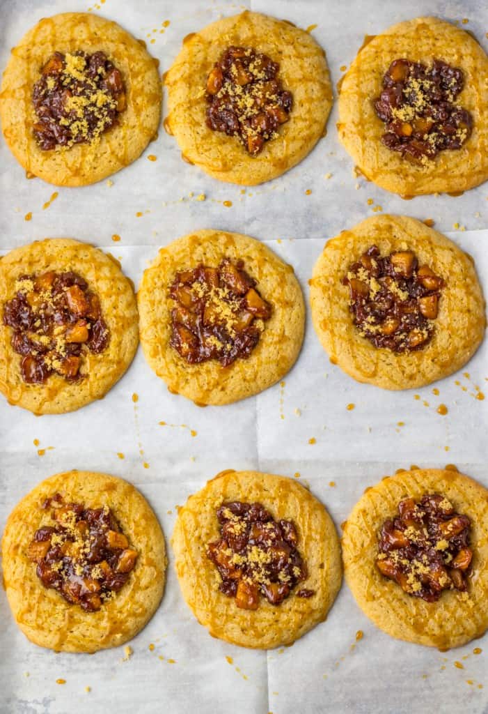 Baked apple spiced cookies with caramel drizzle and a sprinkling of sugar on a parchment paper-lined baking sheet.