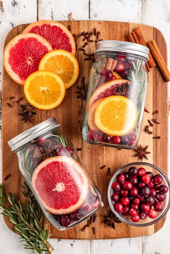 Christmas Simmering Pot Jars on a wooden kitchen board with loose fresh ingredients scattered around.