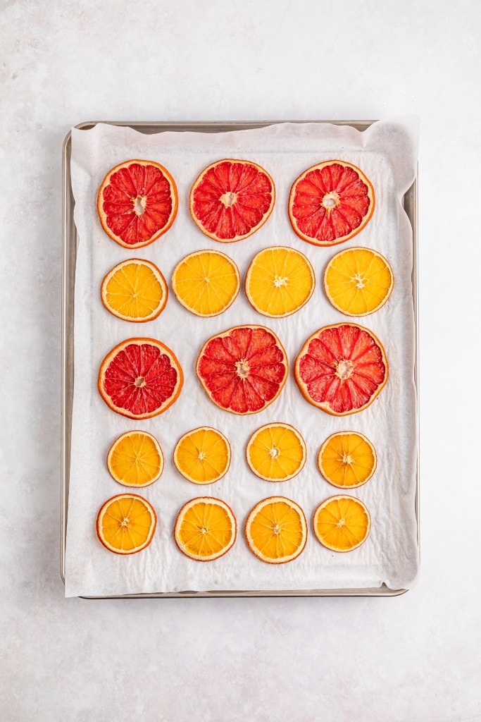 Dehydrated slices of orange and grapefruit on a baking sheet lined with parchment paper.