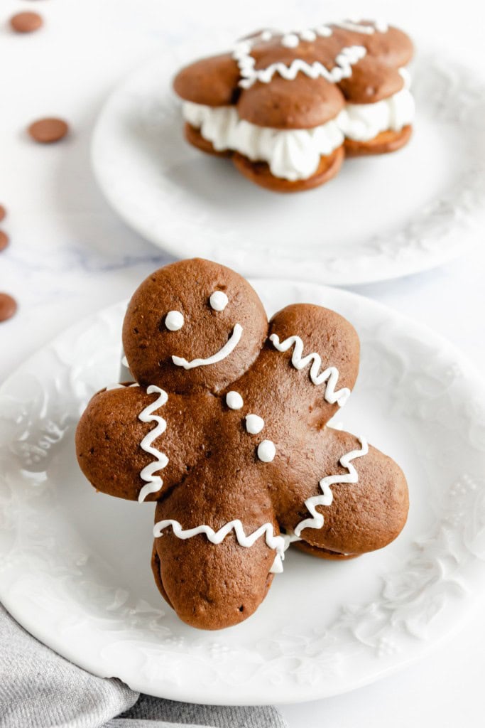 Close up on two gingerbread chocolate whoopie pies on white serving plates on a marble countertop. 