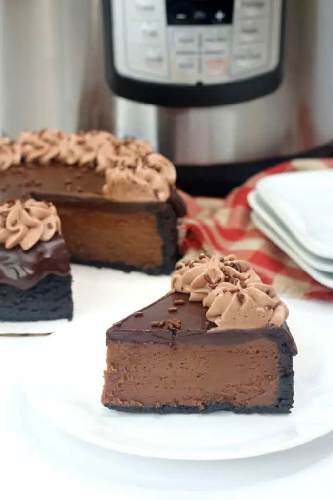 Slice of Instant Pot Nutella Cheesecake on a white serving plate with the rest of the cake in the background together with stacked plates and Instant Pot cooker.