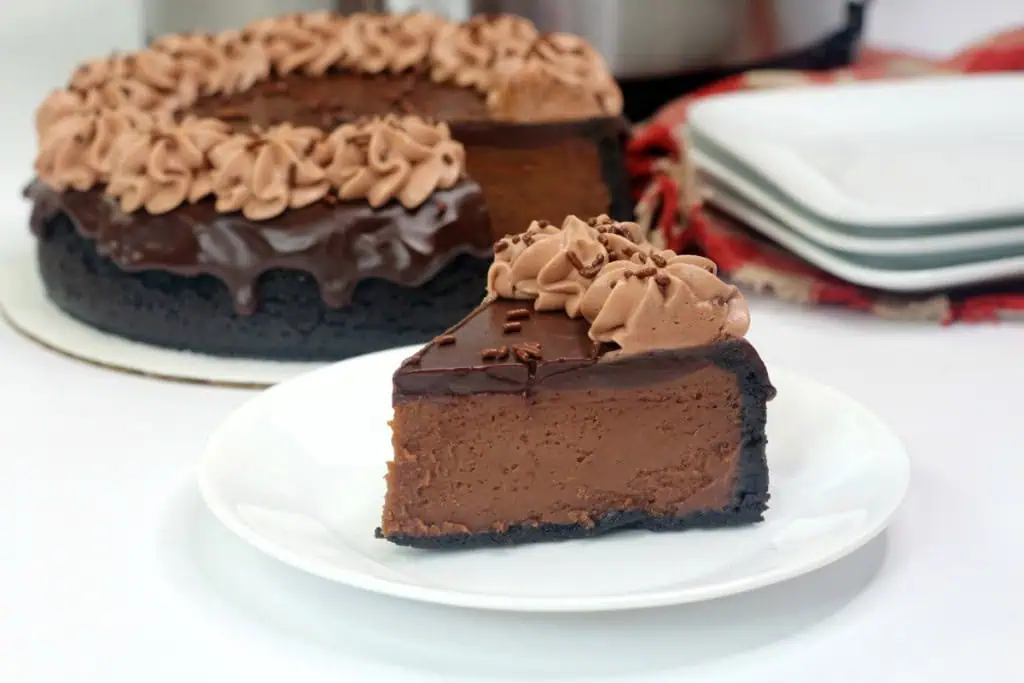 Single slice of Instant Pot Nutella cheesecake on a white serving plate with the whole cheesecake directly behind it.