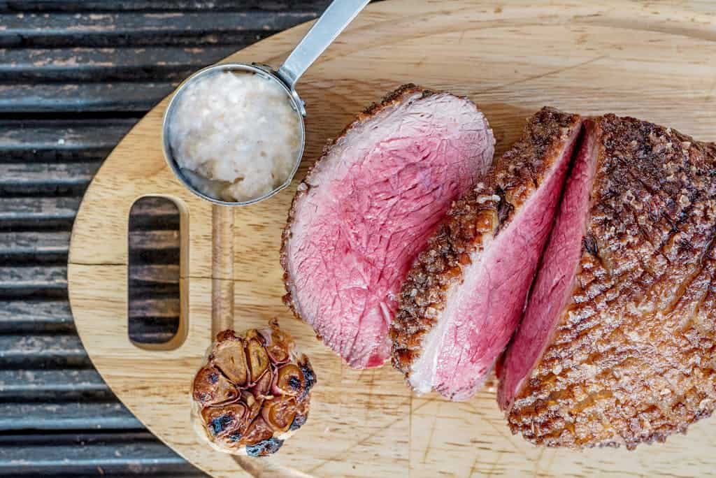 Top view of roasted meat slices with garlic and sauce on a wooden board. Perfect for food lovers.