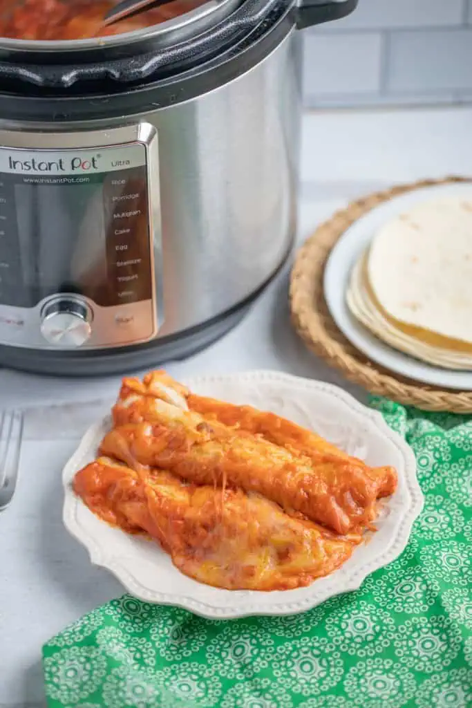 Instant Pot cheesy beef enchiladas on a white plate with the Instant Pot and tortillas in the background.