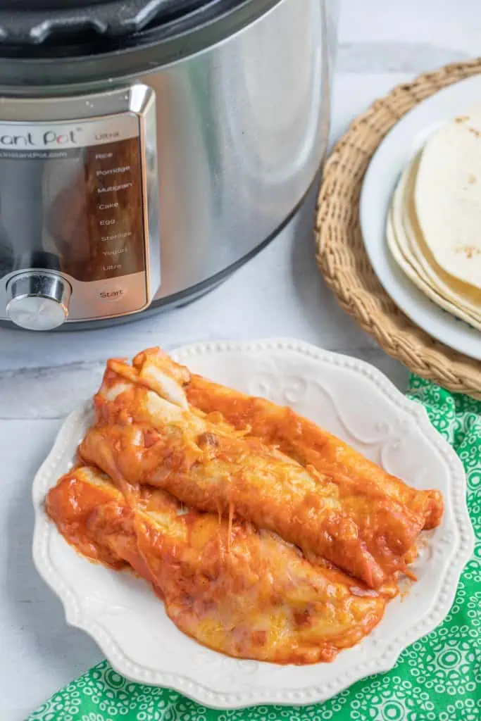 Instant Pot cheesy beef enchiladas on a white plate with the Instant Pot and tortillas in the background.