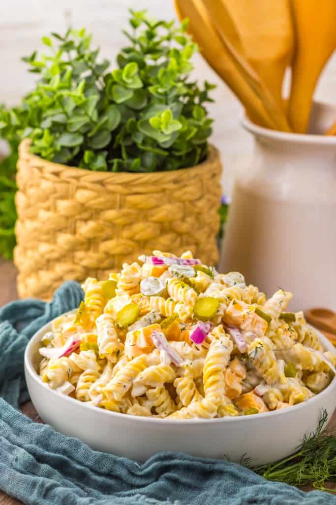 Pickle pasta salad ingredients in a glass bowl with the cream dressing next to it in a separate bowl on a marble countertop. 