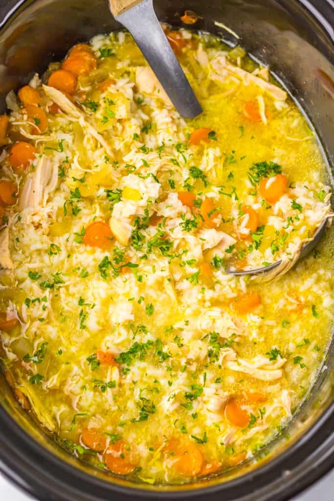 Overhead view of Slow Cooker Chicken and Rice soup in the slow cooker pot with a soup ladle. 