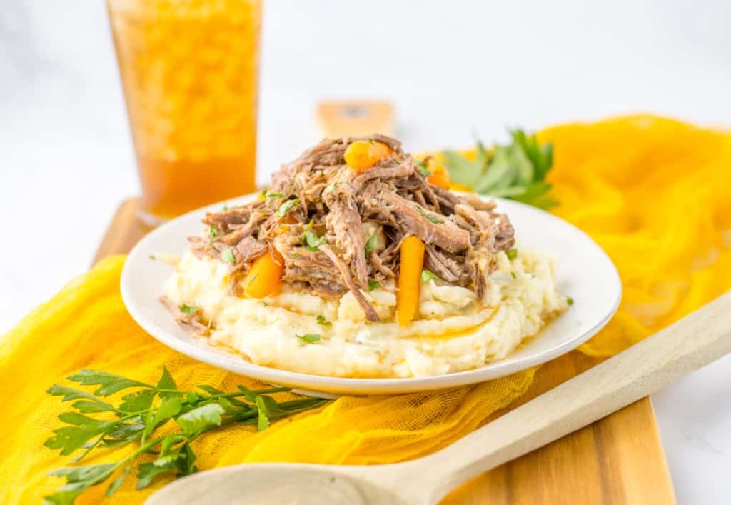 side view of creamy garlic mashed potatoes topped from tender pieces of shredded garlic herb pot roast