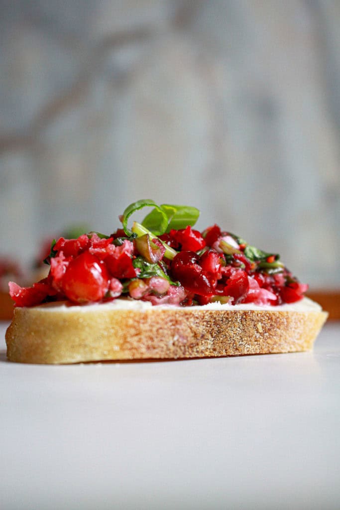 Side view of bruschetta with cream cheese spread and topped with cranberry jalapeno salsa. 