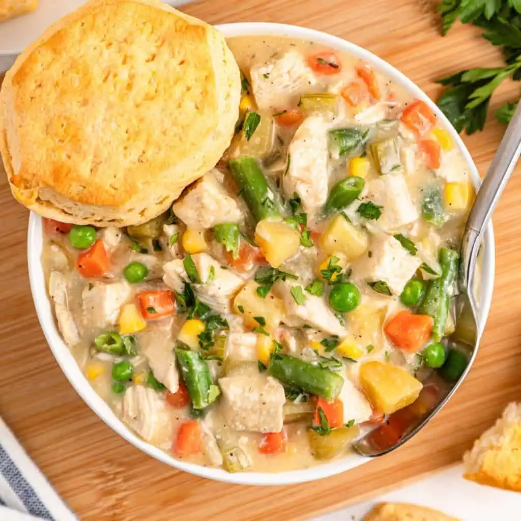 OVERHEAD SHOT OF SLOW COOKER CHICKEN POT PIE IN A WHITE BOWL WITH A BISCUIT ON A WOODEN BOARD