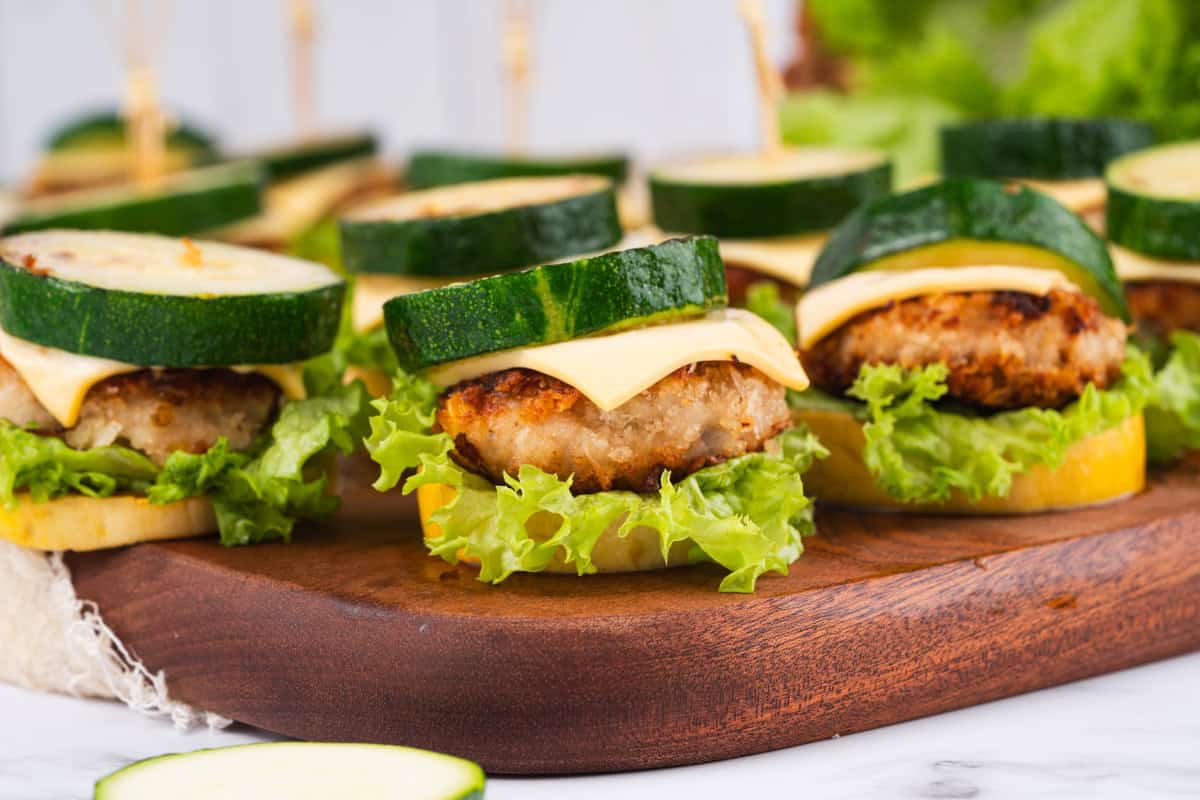 Mini chicken sliders with a slice of cheddar between zucchini rounds and a small piece of lettuce 