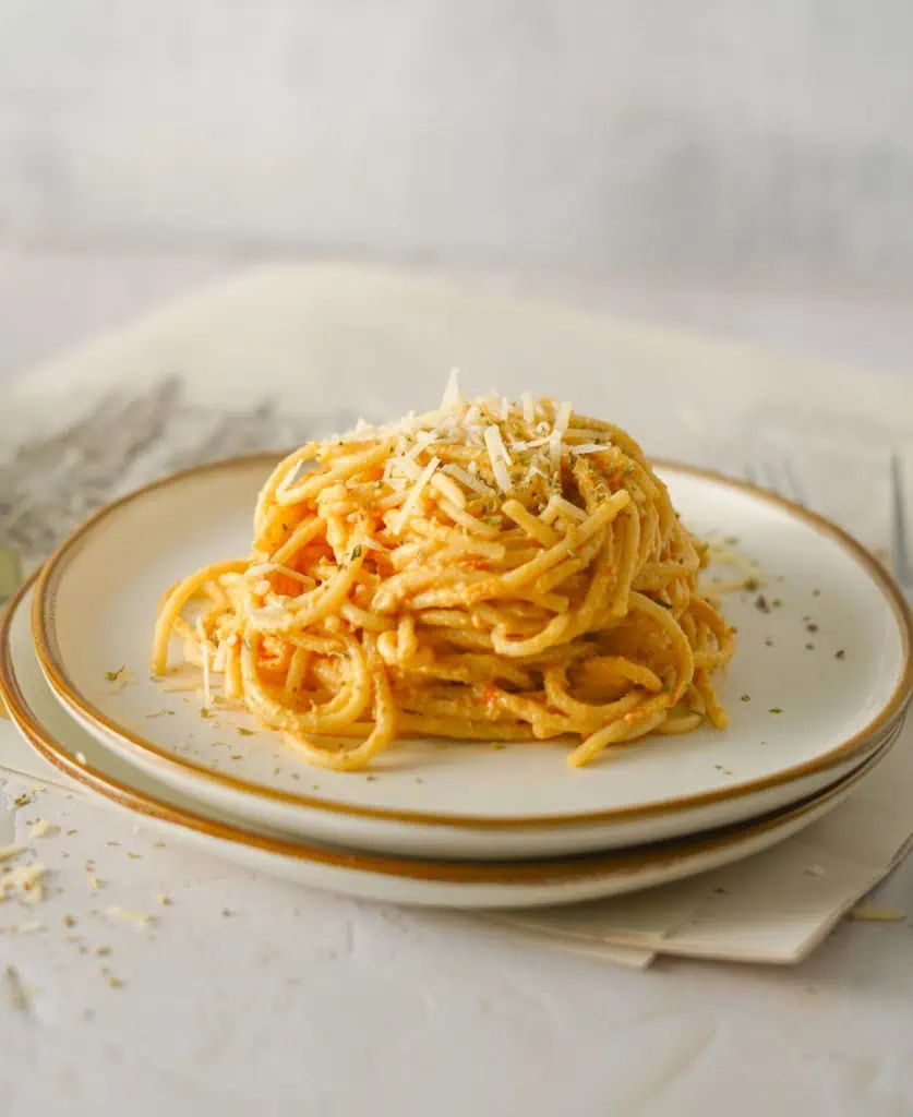 A serving of creamy burrata pasta on a cream plate, topped with a sprinkle of grated Parmesan cheese.