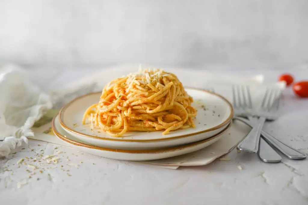 Creamy burrata pasta on a cream serving plate with silver forks, loose cherry tomatoes, and a cream kitchen cloth positioned around the dish.