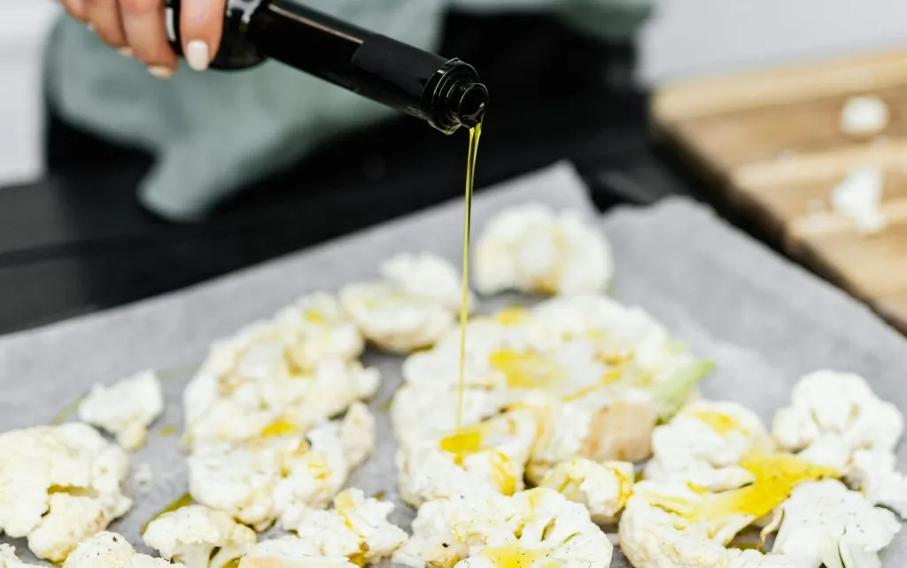 Close-up of a woman preparing a healthy keto meal by pouring olive oil on cauliflower florets.