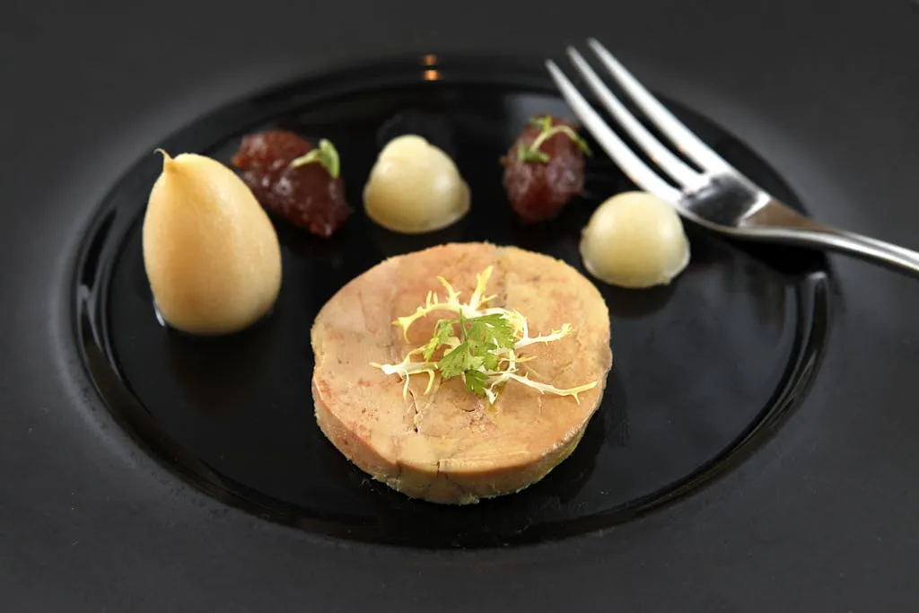 Delicate foie gras served on a black ceramic plate with garnish and puree accompaniments.