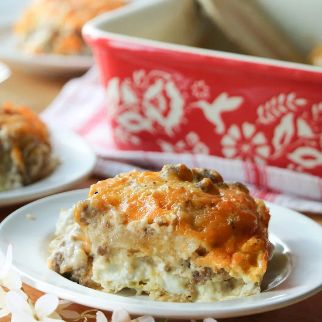 a slice of sausage and gravy casserole on a white plate with a golden cheesy crust topping