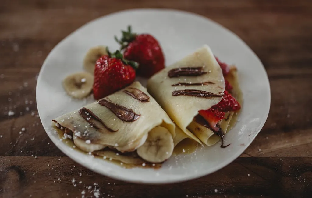 Tasty French crepes topped with fresh strawberries, bananas, and Nutella sauce.