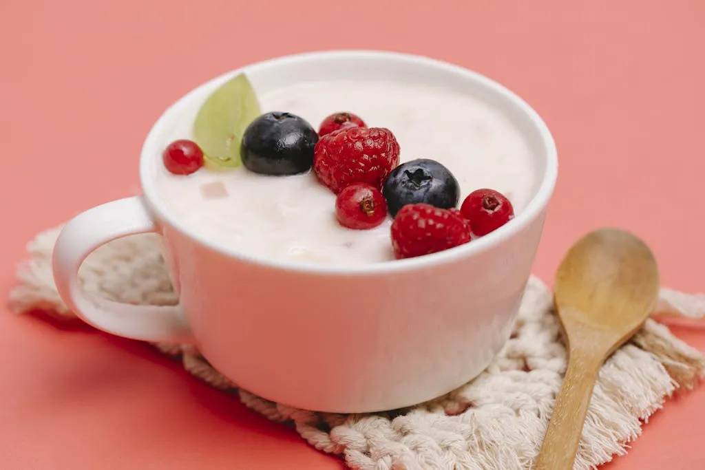 Top view of a white cup filled with yogurt and assorted berries on a pink background.