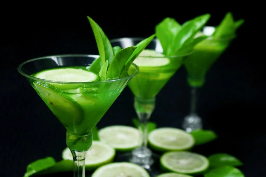 Vibrant green cocktails garnished with lime slices and fresh leaves, perfect for a refreshing drink setup.