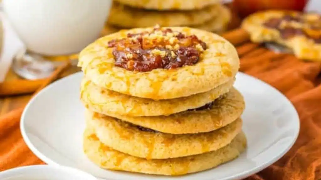 of stack of golden baked apple spiced cookies topped with an apple filling on a white plate next to an orange napkin